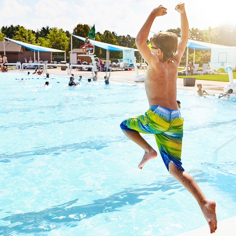 Junge in Badekleidung im Freibad springt in einen Pool.