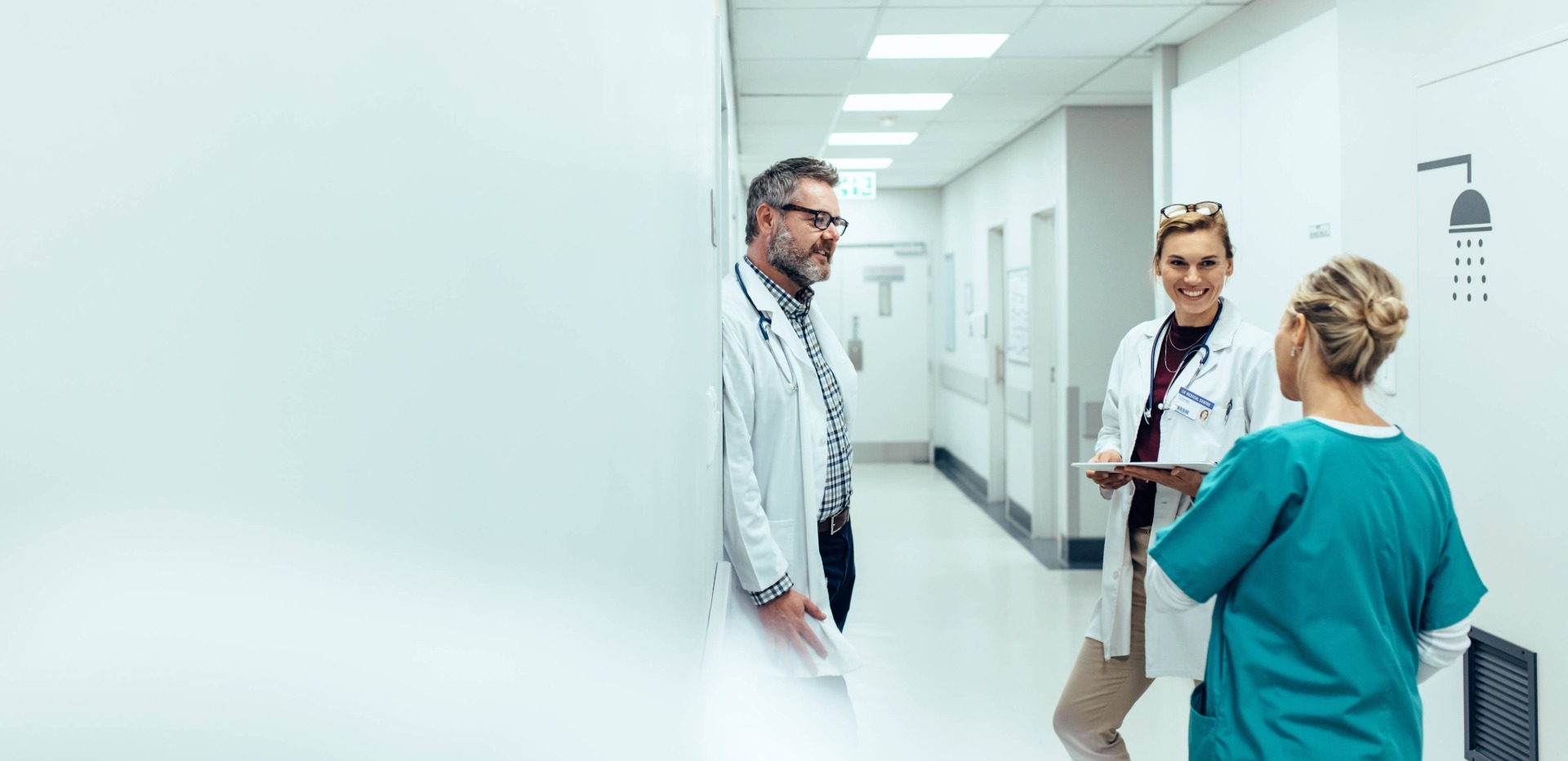 Ein Arzt und eine Ärztin unterhalten sich freundlich mit einer Krankenschwester, im Flur eines Krankenhauses